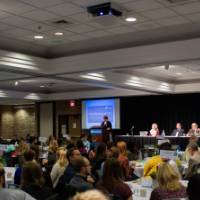 Over 200 attendees are seated at round tables in the Eberhard Center.